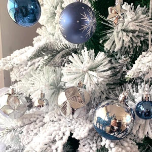 Close-up of blue and silver snowflake ornaments on a white flocked Christmas tree branch