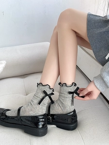 Detail of grey calf-high socks with black bows and ruffled cuffs paired with Mary Janes