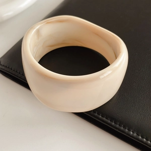 Close-up of a wide cream resin bangle with amber marble texture on black leather background