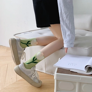 Detail of light green mid-calf socks with white tulip pattern worn with white sneakers