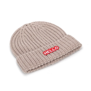 Gros plan du bonnet en tricot marron clair avec écusson HELLO rouge sur le revers