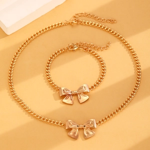 Close-up of golden Cuban chain necklace and bracelet set with bow pendants on warm beige base