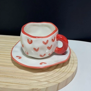 Macro view of ceramic coffee cup set with red hearts and irregular wavy edges on wooden tray