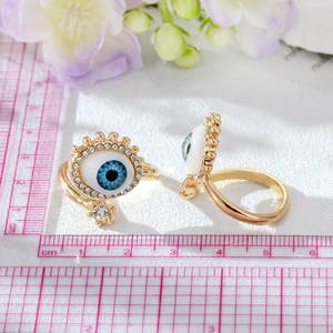 Anelli Evil Eye dorati con cristalli blu su sfondo floreale e scala di misura