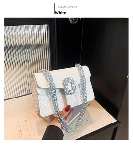 Close-up of white crocodile pattern shoulder bag with rhinestone buckle and silver chain