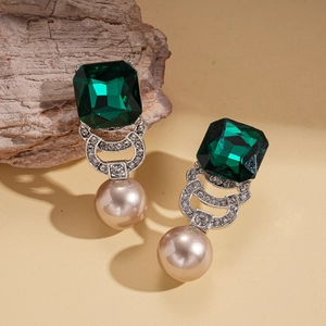 Detail of emerald cut gemstone earrings with vintage champagne pearls on wood background