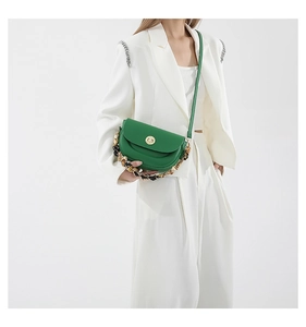 Detail of green saddle bag with gold-tone chain and round metal clasp on model