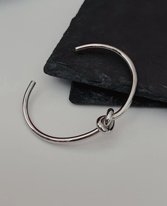 Detailed close-up of a silver knot cuff bracelet on a dark textured stone background