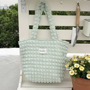Detail of light green bubble textured canvas tote bag with woven brand label on fence