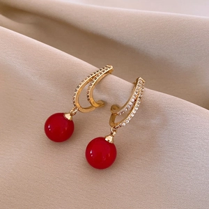 Dettaglio orecchini a cerchio a C dorati con perle rosse su sfondo in tessuto beige