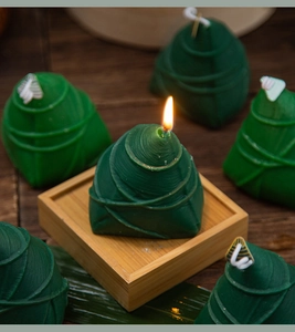 Detail of lit green zongzi-shaped scented candle on a bamboo tray with warm flame