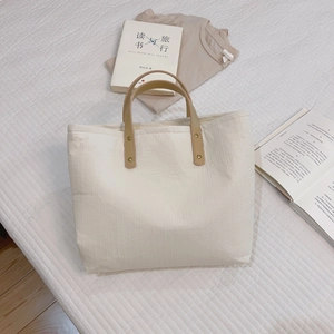 Minimalist beige cotton striped tote bag with brown leather handles on soft white bedding