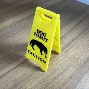Miniature yellow plastic caution sign with dog vomit graphic on a wooden desk