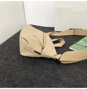 Detail shot of the beige nylon waist bag featuring a broad shoulder strap and side brand tag