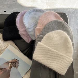 Pile of soft angora wool knitted beanies in pastel colors on a leather sofa surface