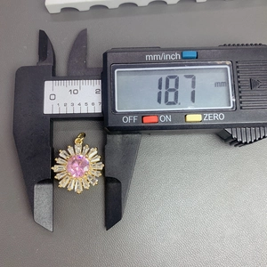 Macro shot of a sunflower pendant with pink crystal being measured with digital calipers