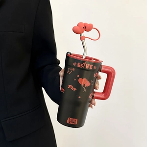 Detail of hand holding a black ceramic mug with red heart balloon straw and love pattern