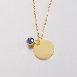 Close-up of a gold round disk pendant necklace with a blue sapphire birthstone charm