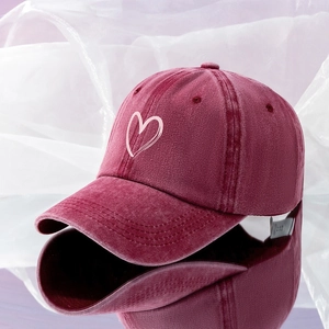 Detailed close-up of a washed burgundy baseball cap with a pink heart embroidery on a mirror