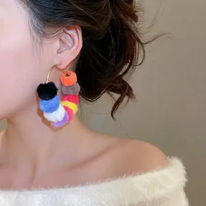 Chic gold hoop earrings with multi-colored pom-poms for a trendy winter fashion look