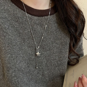 Close-up of star pendant necklace with multi-layered silver chains on grey knitwear