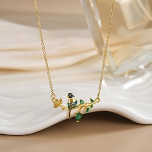 Close-up of bird pendant with blue enamel and green gemstone leaves on a gold chain
