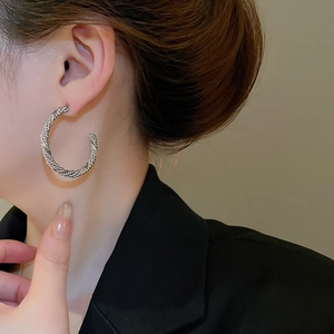 Close-up of a silver twisted C-shaped hoop earring worn on a model for a luxury look