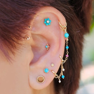 Close-up of gold cartilage piercing set with turquoise stones and vintage studs