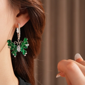 Detail view of silver butterfly earring with green stones worn on a female model