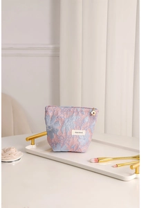 Detail of pink and blue jacquard floral makeup bag on a decorative white tray with golden brush