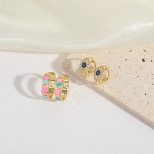 Elegant gold earrings with pink-blue enamel and evil eye charms on beige stone
