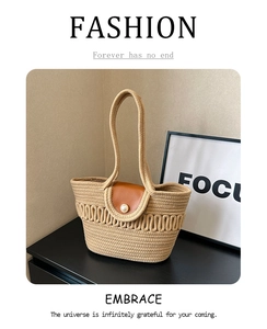 Close-up of hand-woven straw tote bag with brown leather flap and pearl button detail