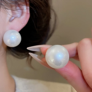Close-up of large round white pearl earrings on model showing glossy finish and size