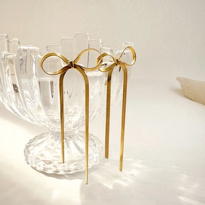 Close-up of golden ribbon bow earrings with long tassel hanging on a glass bowl rim