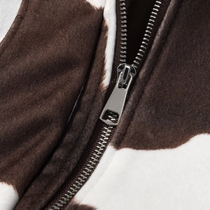 Detailed close-up of cow print fuzzy jacket fabric and metallic silver zipper closure