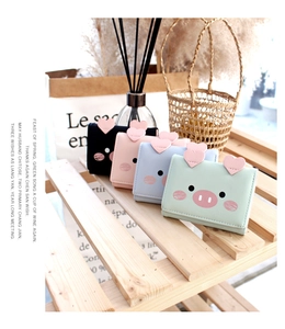 Close-up of cute cartoon pig tri-fold wallets in four pastel colors on a wooden display