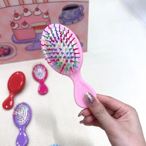 Pink portable mini air cushion hairbrush held in hand to show the small size and scale
