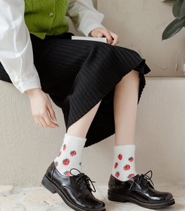 Close-up of fluffy white socks with red strawberry patterns worn by a model on stone steps