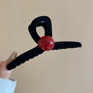 Detailed view of a black velvet claw clip with a glossy red bead accent for hair styling