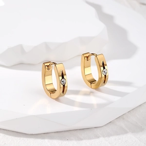 Close-up of gold rectangular earrings with vertical grooves and central zircon stones