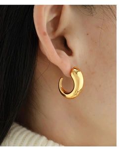 Close-up of chunky polished gold-plated C-shape hoop earring worn by a model