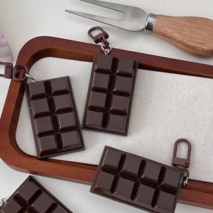 Detailed view of realistic dark chocolate bar keychains on a rustic wooden tray decoration