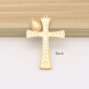 Golden cross necklace pendant with teardrop charm on a light wooden background