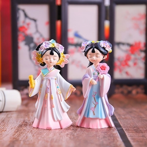 Close-up of ancient style lady figurines with scrolls and fans on a wooden table