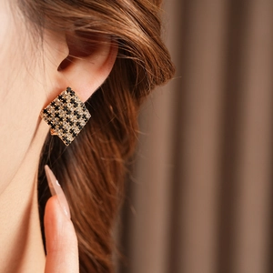 Vue détaillée de boucles d'oreilles dorées avec motif à damier noir et blanc serti de diamants