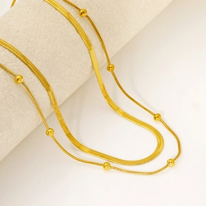 Double-layered golden herringbone and bead chain necklace on jewelry display