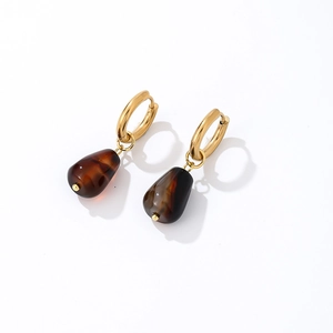 Close-up of golden hoop earrings with amber teardrop resin pendants on white background
