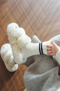 Close-up of soft white plush slippers and striped knit wool socks on a wooden floor