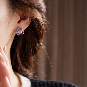 Close-up of a model wearing minimalist silver stud earrings with a round purple zircon