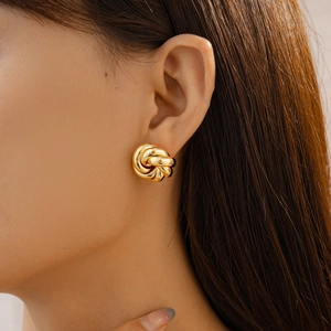 Close-up of a model wearing a glossy gold twisted knot stud earring with a metallic finish